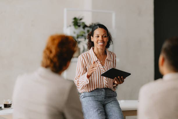 A senior HR professional leading a discussion with colleagues around a meeting table in a bright modern office
